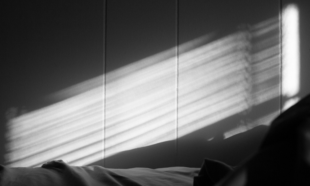 Soft light leaks through window blinds onto a bedroom wall